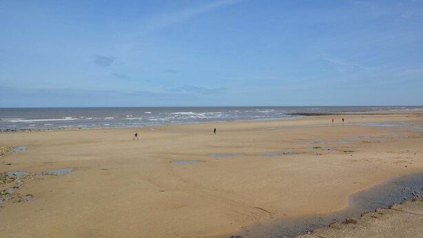 Een breed zandstrand met een heldere lucht en een rustige zee.