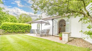 Een wit huis met een terras, een tafel met stoelen en een potplant.