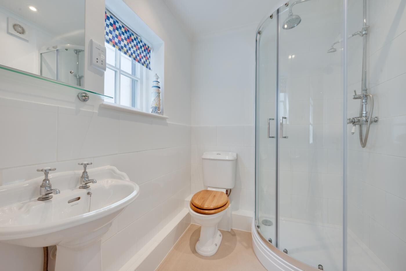 Et badeværelse med et glasvægshus, en hvid vask med to haner og et toilet med træsæde.