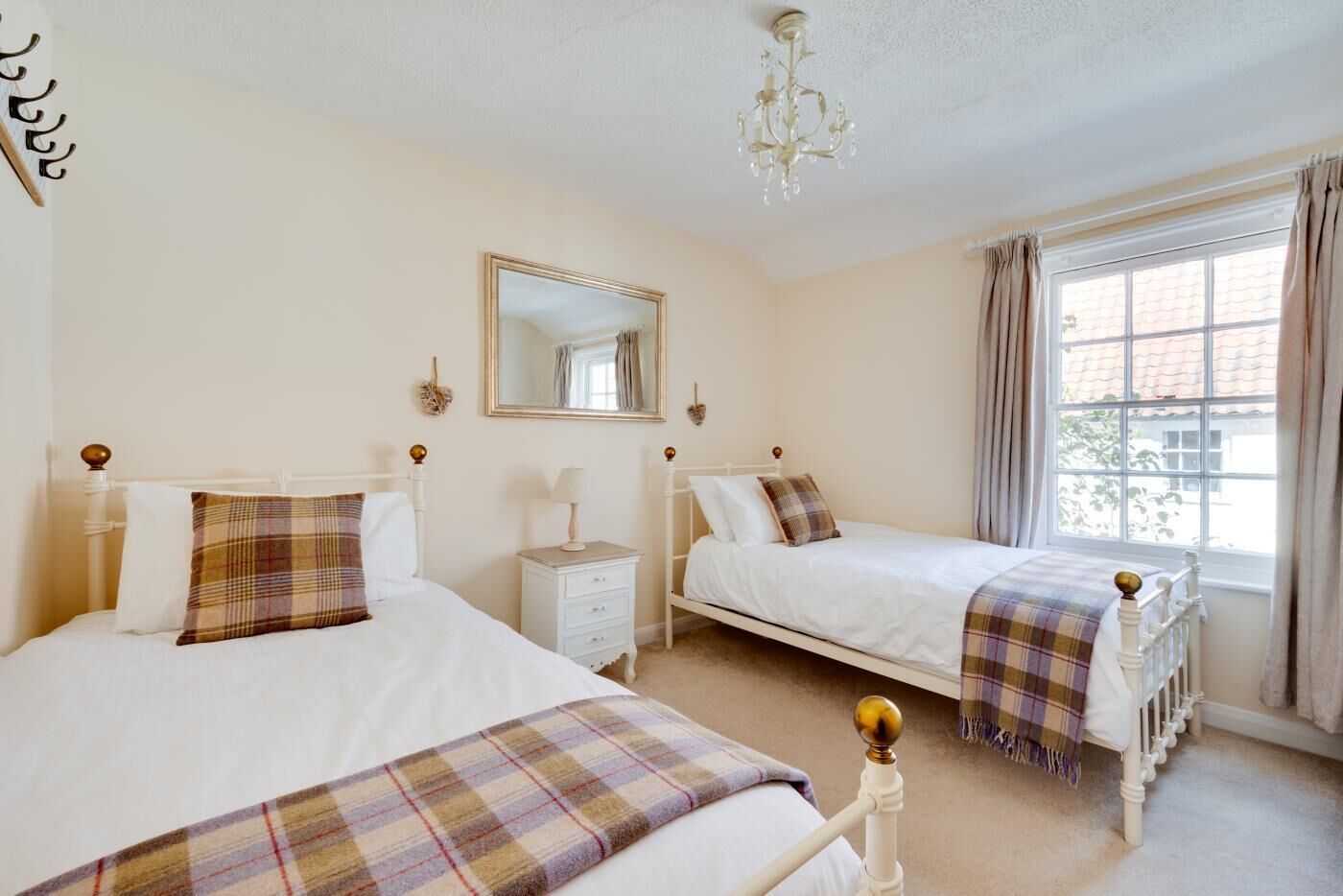 A bedroom with two single beds, a bedside table with a lamp, a mirror, and a window with curtains.