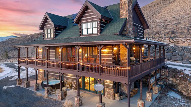Eine Lodge mit Natursteinfassade, einer Holzterrasse und einem Balkon mit Lichterketten.