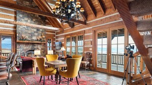 Ein rustikales Lodge-Interieur mit Kamin aus Stein, Holzbalken und großen Fenstern mit Blick auf die Berge.