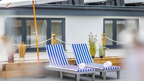 A modern outdoor lounge area with two striped lounge chairs, a wooden planter with plants, and a rope barrier. - 3 Bed in Shanklin (oc-h33403) (Shanklin)
