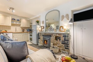 Un salon chaleureux avec une cheminée, une cuisine aux meubles blancs et un coin repas avec une table mise pour deux personnes.