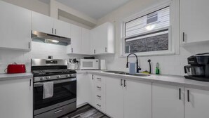 A modern kitchen with white cabinets, stainless steel appliances, and a window with blinds. - Furnished 2BR w/Parking – Mid-Term Stay Near Falls (Niagara Falls)