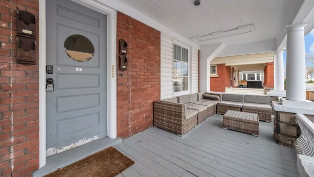 A covered porch with wicker furniture and a grey door. - Furnished 2BR w/Parking – Mid-Term Stay Near Falls (Niagara Falls)