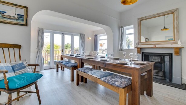 Un coin repas avec une table en bois dressée pour six personnes, des bancs dotés de coussins à motifs, une chemin ée et un grand miroir au mur.