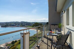 Un balcon avec une table dressée pour le dîner, donnant sur une zone côtière avec une plage et une vue sur le paysage urbain.