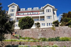 Un immeuble à plusieurs étages doté de balcons, de murs de soutènement en pierre et d’un jardin aménagé.