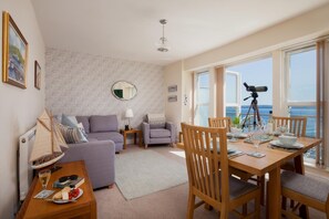 A modern living room with a dining area, a large window with a telescope, and a view of the sea. - 2 Bed in Torquay (oc-9marco) (Torquay)