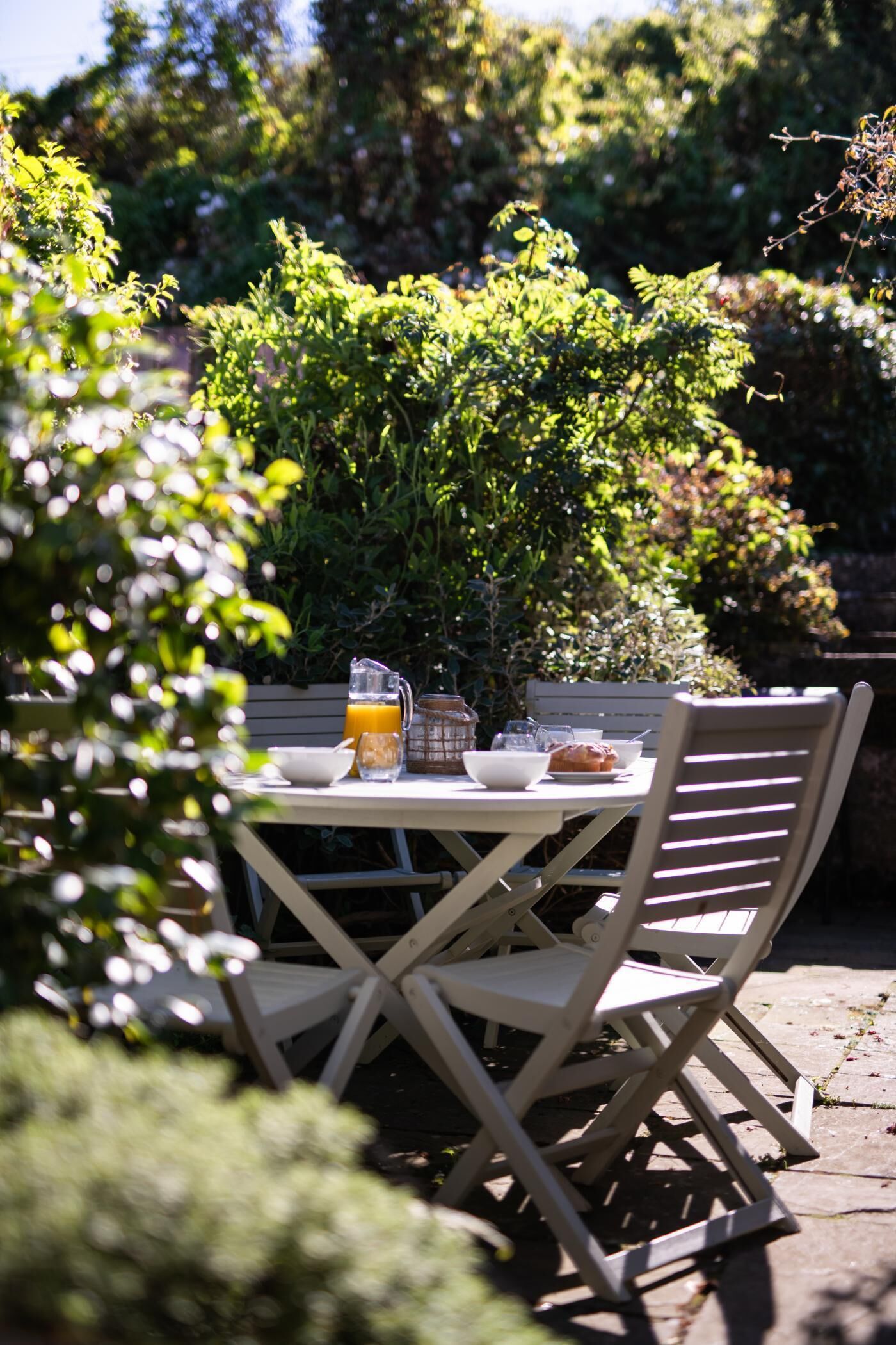 An outdoor dining area with a table set for two, surrounded by greenery.
