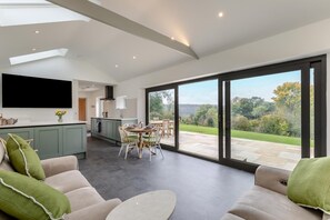 A modern kitchen with a dining area and a large sliding glass door leading to a garden. - 2 Bed in Minchinhampton (oc-w33358) (Minchinhampton)
