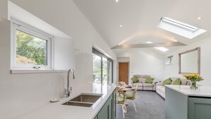 Een moderne keuken met een groot raam, een eethoek met een tafel en stoelen, en een zithoek met een bank en een spiegel.