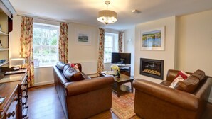 A living room with leather sofas, a television, a fireplace, and a large window with curtains. - 2 Bed in Beaumaris (oc-wai206) (Beaumaris)
