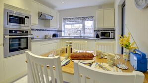 A modern kitchen with white cabinetry, a dining table set for four, and a large loaf of bread on the table. - 2 Bed in Beaumaris (oc-wai206) (Beaumaris)