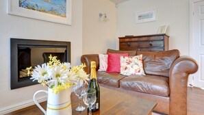 A living room with a leather sofa, a coffee table with a bottle of champagne and glasses, a vase with flowers, and a fireplace. - 2 Bed in Beaumaris (oc-wai206) (Beaumaris)