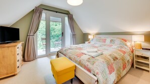 Ein Schlafzimmer mit einem Bett, einem Fernseher, einer Holzkommode, einem gelben Hocker und einem Balkon mit Vorhängen.