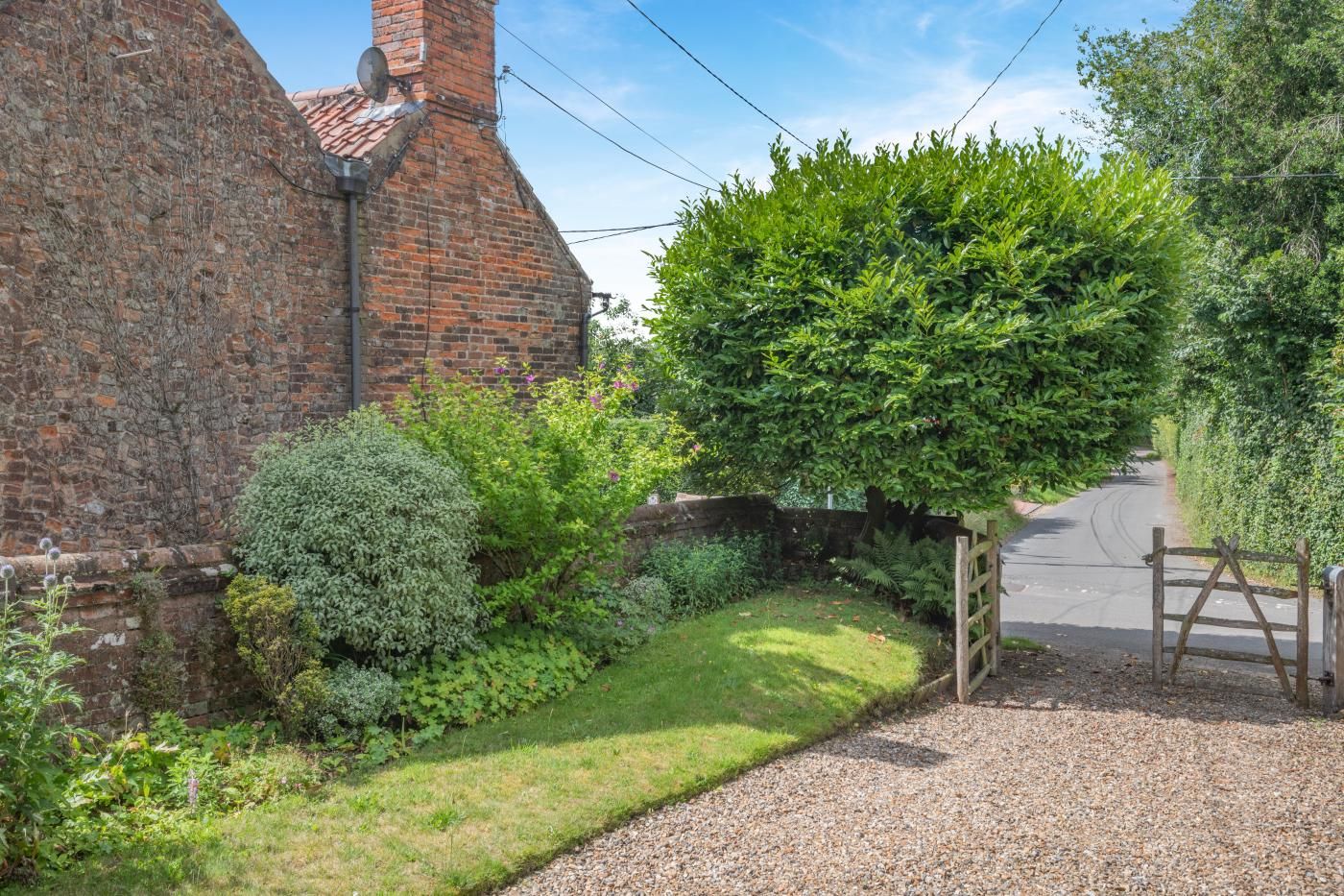 A rural property with a brick building, a gravel driveway, and a wooden gate.