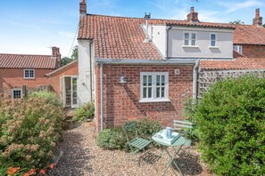 A brick house with a tiled roof, a small garden with a table and chairs, and a neighboring house. - 1 Bed in Swanton Novers (oc-1747) (Swanton Novers)