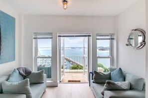 A spacious living room with two sofas, a large painting, and a view of the sea through open doors. - 2 Bed in Torquay (oc-maribh) (Torquay)