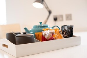 Un coin cuisine comprenant une bouilloire turquoise, une machine à café et un plateau avec des dosettes de café et des en-cas.