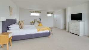 Un dormitorio con cama, mesita de noche, cómoda, televisor y dos ventanas.
