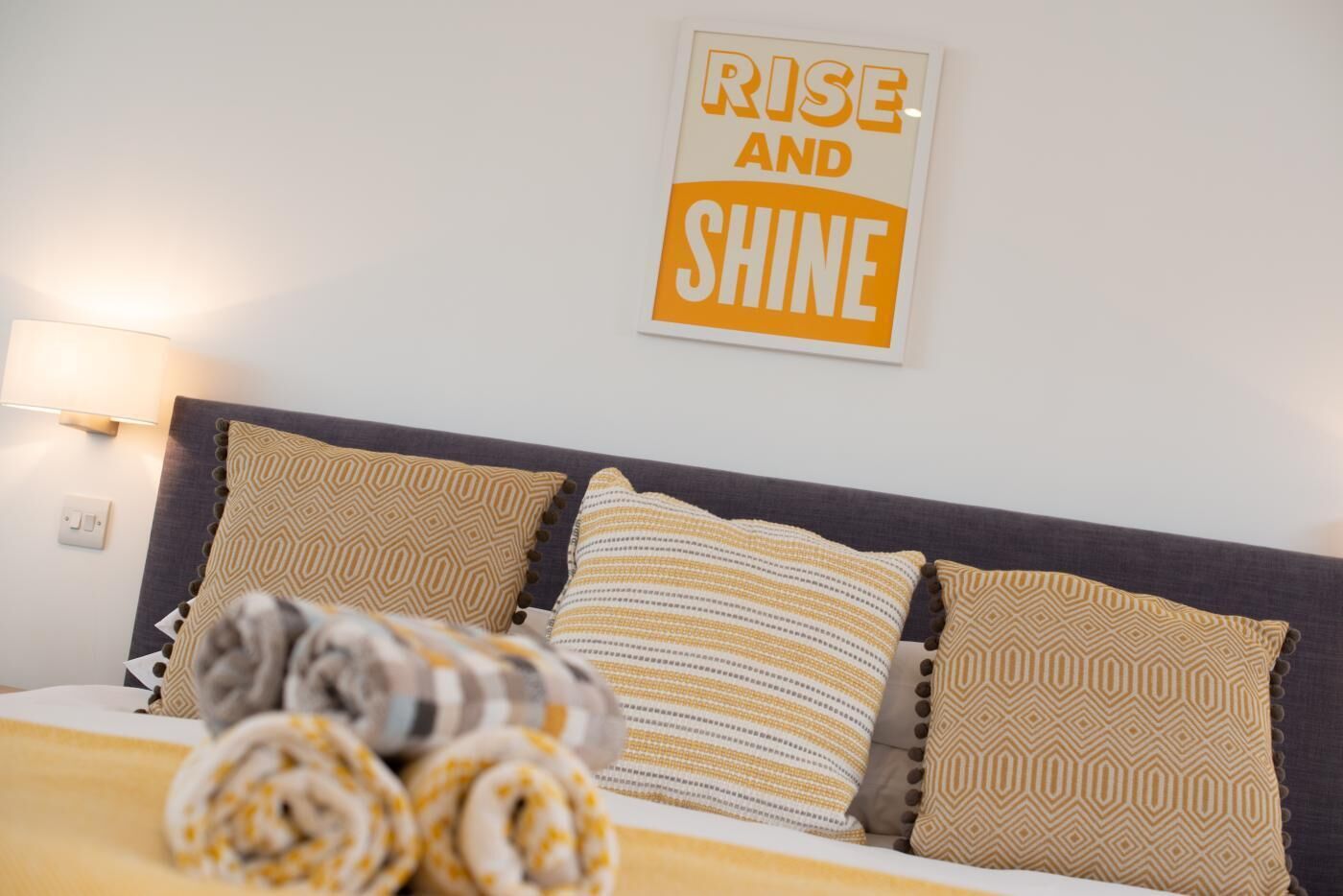 Una cama bien hecha con almohadas estampadas y una cita motivadora en la pared.