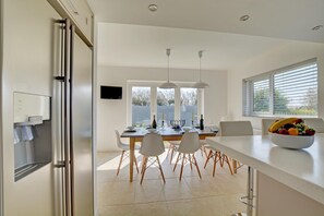 A modern kitchen with a dining area, a water dispenser, and a fruit bowl on the counter. - 6 Bed in Constantine Bay (oc-p00571) (Constantine Bay)