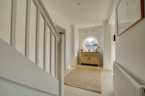Un couloir avec un escalier, une fenêtre ronde, une armoire et un radiateur.