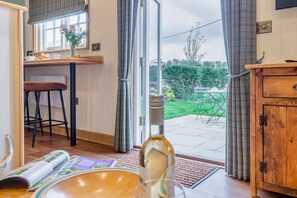 A kitchen with a wooden counter, a bar stool, a window with curtains, and a view of a garden. - 1 Bed in Holkham (oc-s33494) (Holkham)