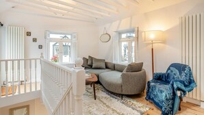 A cozy living room with a sofa, a blue armchair, a lamp, and a view through a window. - 2 Bed in Lynton (oc-s33456) (Lynmouth)