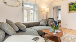 A modern living room with a sectional sofa, a round coffee table, and a large window with shutters. - 2 Bed in Lynton (oc-s33456) (Lynmouth)