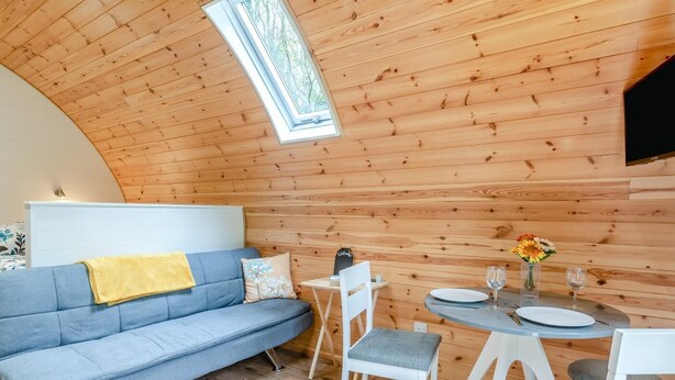 Una habitación acogedora con techo abovedado, un sofá, una mesita con un florero y una silla.
