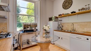 Et moderne køkken med et glasbord, kaffemaskine, en Bosch opvaskemaskine og et vindue med udsigt til grønne omgivelser.