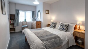A bedroom with a bed, bedside tables, a dresser, a chair, a bookshelf, a window with curtains, and a mirror. - 2 Bed in Reepham (oc-1755) (Reepham)