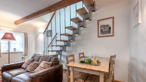 A cozy living room with a brown leather sofa, a wooden dining table with chairs, and a staircase with exposed metal railings. - 2 Bed in Reepham (oc-1755) (Reepham)