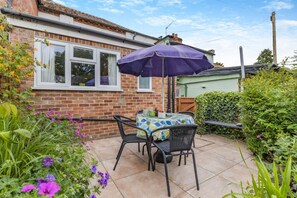 A patio with a table and chairs, a purple umbrella, and a brick house in the background.