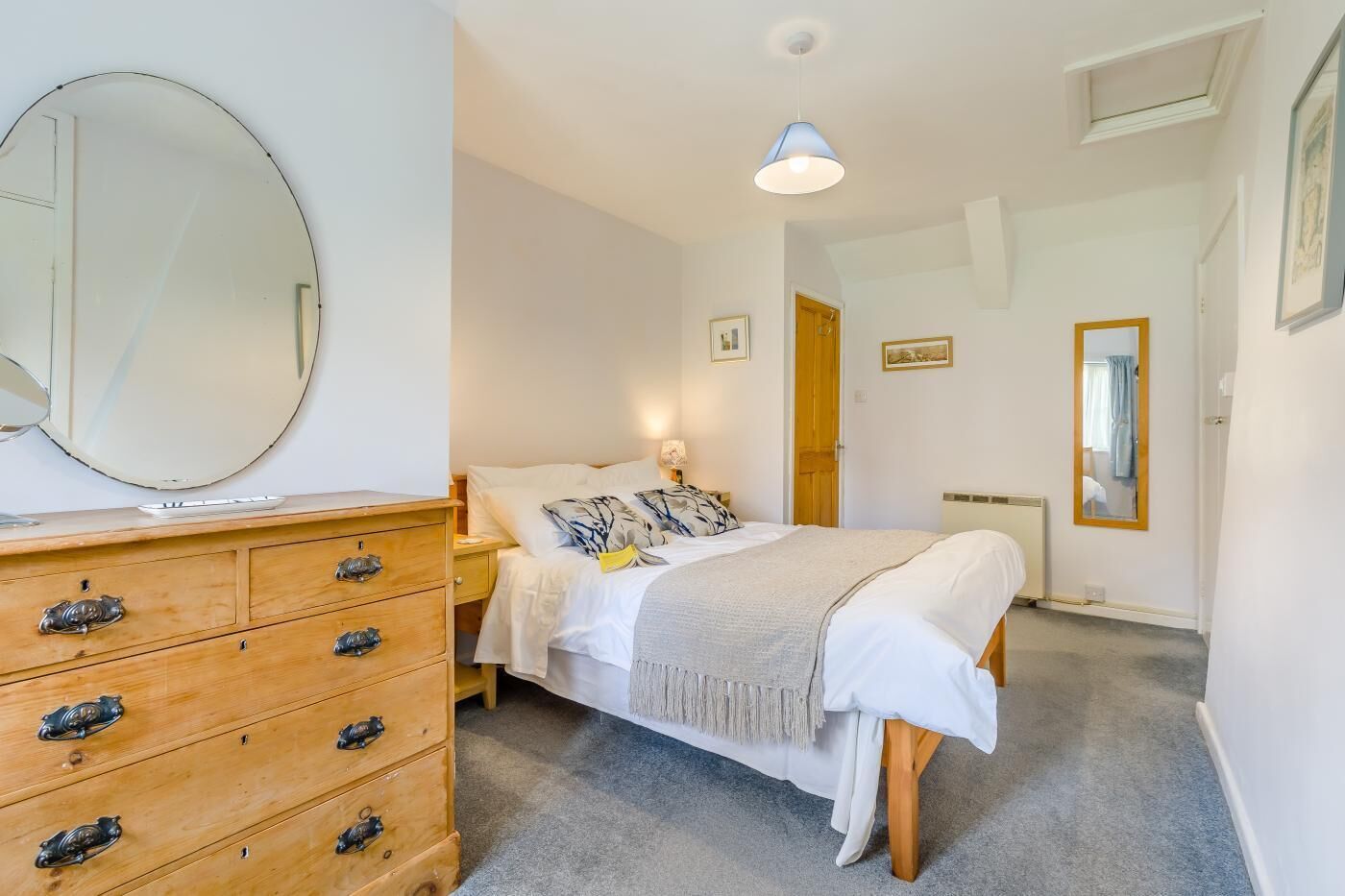 A bedroom with a bed, a dresser with drawers, a mirror, a lamp, and a door leading to another room.