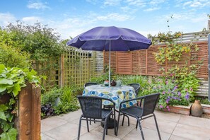 An outdoor patio with a table and chairs, a purple umbrella, and a variety of plants.