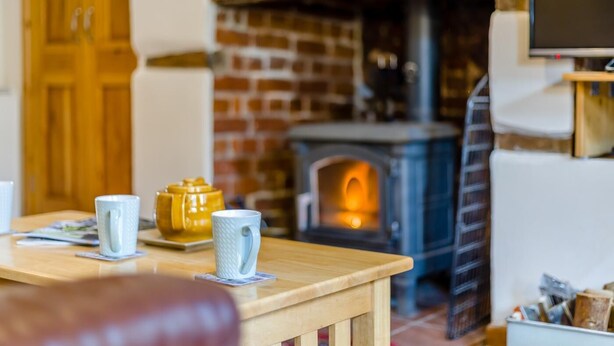 A cozy living room with a brick fireplace, a wooden table with mugs, and a television on a stand. - 2 Bed in Reepham (oc-1755) (Reepham)