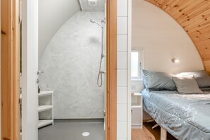 A compact, modern bedroom with a curved ceiling, a built-in shower, and a bed with a blue bedspread.