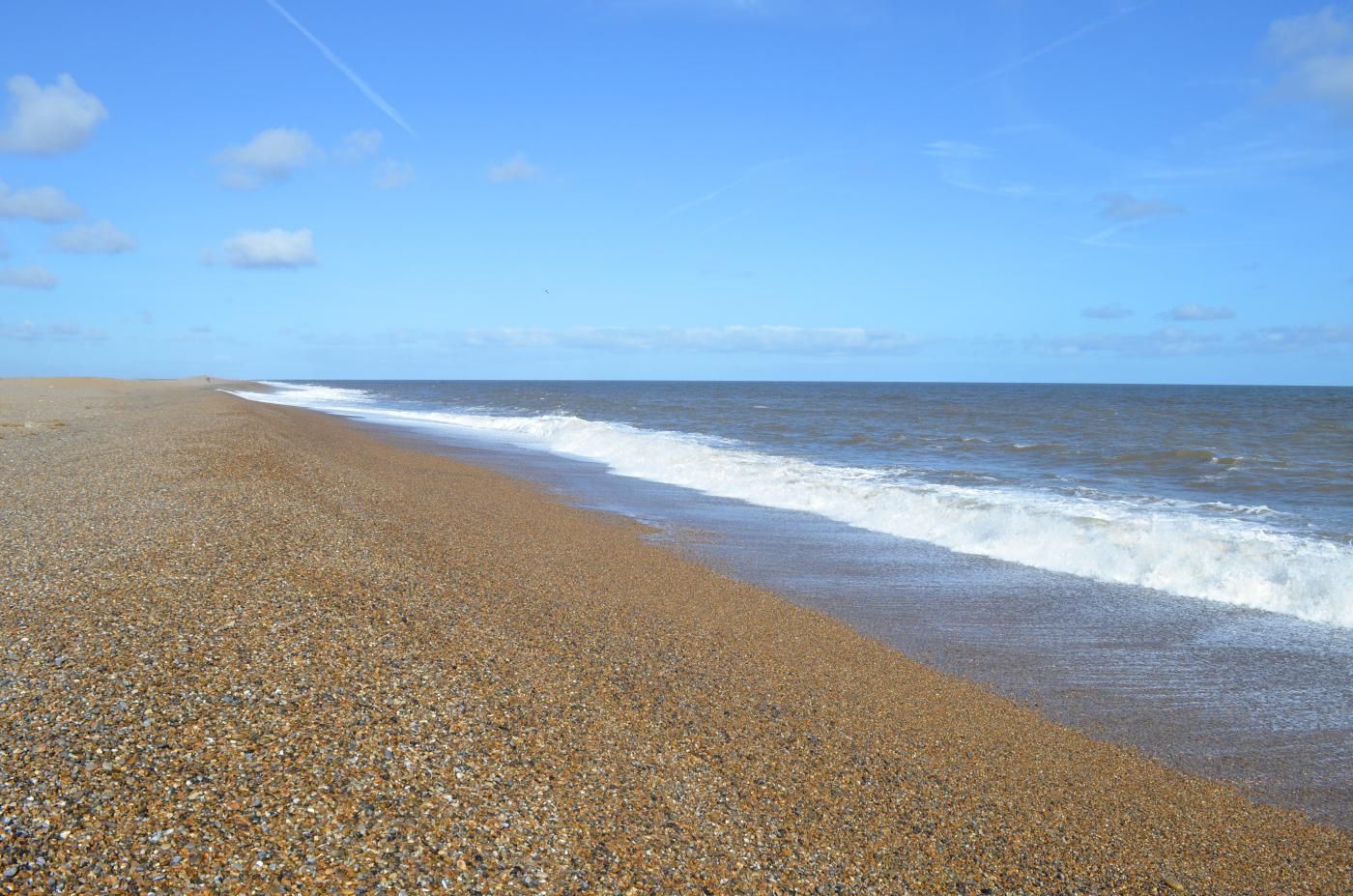 A pebbled beach with waves approaching the shore under a clear sky.