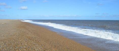 A pebbled beach with waves approaching the shore under a clear sky.