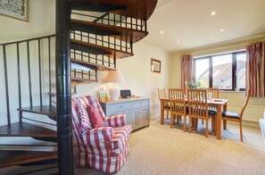 A staircase with a wooden finish, a dining area with a table and chairs, and a seating area with a patterned sofa. - 3 Bed in Salthouse (oc-1753) (Salthouse)
