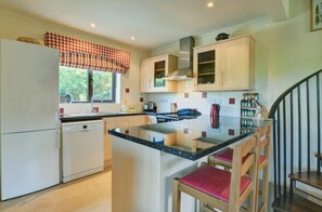 A kitchen with a central island, a refrigerator, a dishwasher, wooden cabinets, and a window with a checkered valance. - 3 Bed in Salthouse (oc-1753) (Salthouse)
