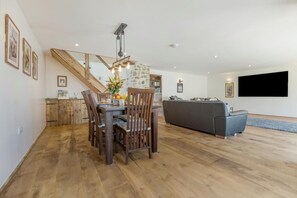 Ett rymligt vardagsrum med ett matbord, stolar, en soffa, en TV och en trappa.