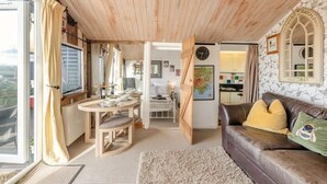 Ein gemütliches Wohnzimmer mit Holzbalkendecke, ein Essbereich mit rundem Tisch und eine durch eine offene Tür sichtbare Küche.
