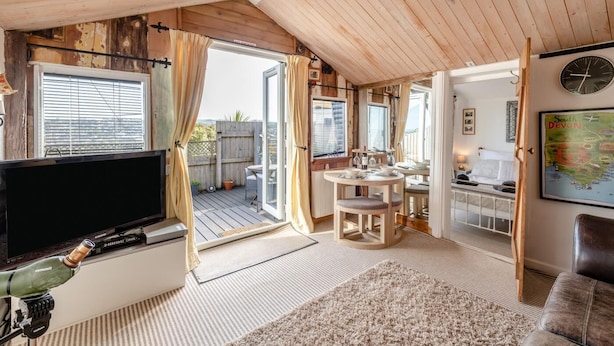 Ein gemütliches Zimmer mit Fernseher, Holzboden, Essecke und einem Bett.