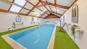 Una piscina interna con struttura a soffitto in legno, bordi in erba sintetica e tetto in vetro trasparente.