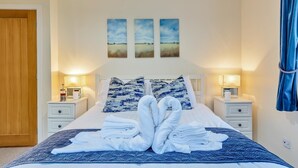 Un letto rifatto con cura, asciugamani, comodini con lampade e tre dipinti di paesaggi appesi al muro.